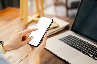 Ahşap masada boş ekranlı akıllı telefon kullanan bir kadının görüntüsü. Kadın eli ve cep telefonunun yakın fotoğrafını çek