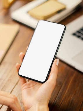 Ahşap masada boş ekranlı akıllı telefon kullanan bir kadının görüntüsü. Kadın eli ve cep telefonunun yakın fotoğrafını çek