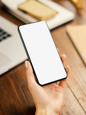 Ahşap masada boş ekranlı akıllı telefon kullanan bir kadının görüntüsü. Kadın eli ve cep telefonunun yakın fotoğrafını çek