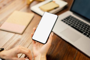 Ahşap masada boş ekranlı akıllı telefon kullanan bir kadının görüntüsü. Kadın eli ve cep telefonunun yakın fotoğrafını çek