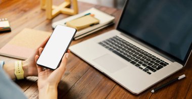 Ahşap masada boş ekranlı akıllı telefon kullanan bir kadının görüntüsü. Kadın eli ve cep telefonunun yakın fotoğrafını çek