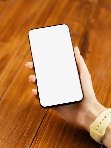 Ahşap masada boş ekranlı akıllı telefon kullanan bir kadının görüntüsü. Kadın eli ve cep telefonunun yakın fotoğrafını çek