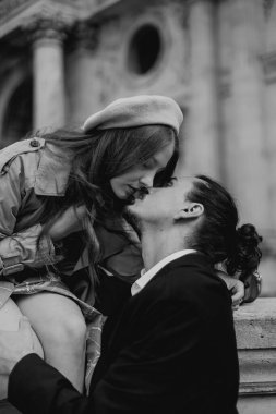 Aşık bir çift Paris sokaklarında yürüyor, ceketli ve takım elbiseli bir adam, bereli bir kız ve sonbaharda siyah beyaz bir trençkot giymiş bir kız.