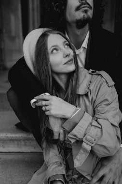 Aşık bir çift Paris sokaklarında yürüyor, ceketli ve takım elbiseli bir adam, bereli bir kız ve sonbaharda siyah beyaz bir trençkot giymiş bir kız.