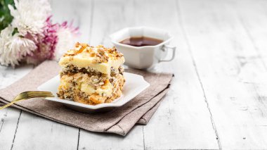 Bir parça ev yapımı Kyiv Keki ya da Beyaz Tabakta Dacquoise Keki. Arkaplanda çay ve çiçek var.