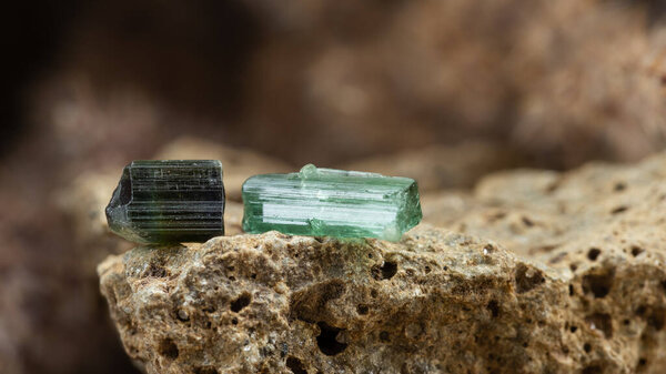 Two pieces of Raw Blue and Green Tourmaline Crystal on Rough Stone Background in Natural Light
