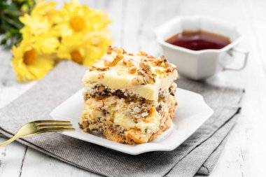 Bir parça ev yapımı Kyiv Keki ya da Beyaz Tabakta Dacquoise Keki. Arkaplanda çay ve çiçek var.