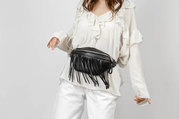 stock image White Woman Wearing White Jeans, Blouse with Frills and Crossbody Black Leather Belt Bag with Decorative Fringe over Grey Background