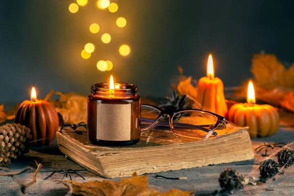 Karanlık Kehribar Cam Kavanozunda Soya Cila Mumuyla Cadılar Bayramı Mock Up için Boş Etiket. Balkabağı şekilli mumlar koni, yaprak, eski kitap ve gözlüklü. Arkaplanda Bokeh Işıkları