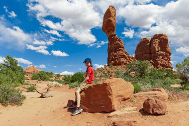 Boy Resting near Balanced Rock in Arches National Park in Utah. Landscape Photo in the Summer clipart