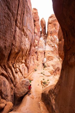 Genç bir yürüyüşçü çocuk ateşli fırın patikasında bir kayaya tırmanıyor, Arches Ulusal Parkı, Utah, bu ikonik Amerikan manzarasının maceraperest ruhunu ve çarpıcı kızıl kaya oluşumlarını sergiliyor.