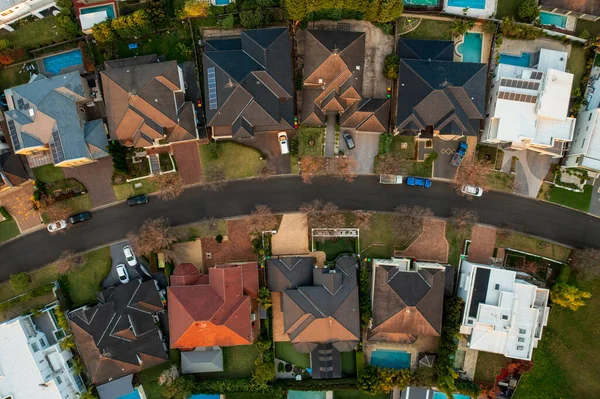 Aerial top down view of upmarket houses on a curved street in the fading winter sun in outer suburban Sydney, Australia.