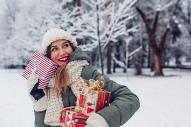 Noel hediyeleri taşıyan mutlu genç bir kadının portresi. Dışarıdaki karlı kış parkında hediye kutuları. Bayram şenliği. Boşluk. Model