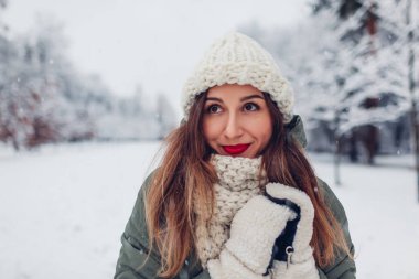 Karlı kış parkında, sıcak örgü giysiler giymiş, kırmızı ruj sürmüş, kar altında manzaranın tadını çıkaran mutlu genç bir kadının portresi..