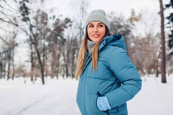 Portrait of young woman walking in snowy winter park wearing blue down jacket. Warm clothes for cold frosty weather. Space
