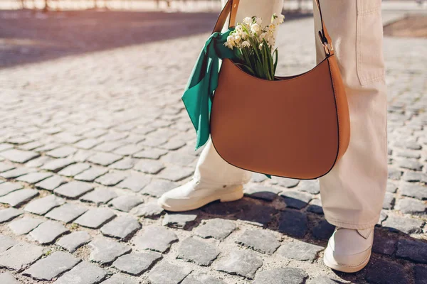 結びスカーフや靴と女性の革ハンドバッグのクローズアップ 女性は白い春の花の花束を屋外で茶色の財布を持っています スタイリッシュなアクセサリー スペース — ストック写真