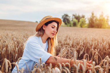 Yaz tarlasında buğday toplayan genç bir kadının portresi. Gün batımında hasır şapka takıyor. Manzaranın tadını çıkaran kız. Genç çiftçi hasatı kontrol ediyor