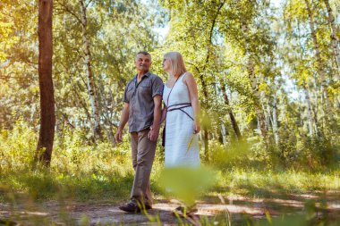 Senior family couple walking outdoors in summer forest. Elderly people holding hands. Romantic date. Man and woman enjoy landscape