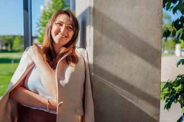 Güneşli ofiste duvarın yanında duran mutlu iş kadını. Genç, gülümseyen patron müdürü dinleniyor. Kadın takım elbise giyiyor. Boşluk