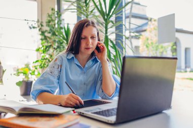 Genç bayan öğretmen Laptop bilgisayarı kullanarak ofiste çalışmaya hazırlanıyor. Tablete notlar yazan kadın