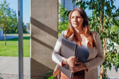 Takım elbiseli kendine güvenen bir işçi dizüstü bilgisayarı pencerede tutuyor. Kafkasyalı genç iş kadını pencerenin yanında duruyor..