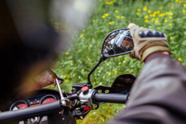 Motosikletçi açık havada motosiklet aynasına bakarak uyum sağlıyor. Yaz ormanında deri ceketli ve kask takan bir adam..