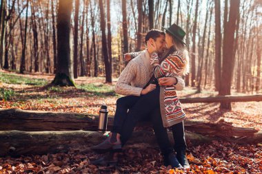 Sonbahar ormanlarında termostan çay içen genç bir çiftin portresi. Bagajda oturan erkek ve kadın, sonbahar manzarasının tadını çıkarıyorlar.