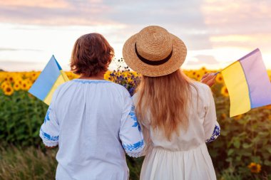 Kadın vatanseverlerin arka planında Ukrayna bayrakları var. Gün batımında ayçiçeği yaz tarlasında ulusal kıyafetler giyiyorlar. Ukrayna 'nın Bağımsızlık Günü. Anne ve kızı kutlama yapıyor. Aile