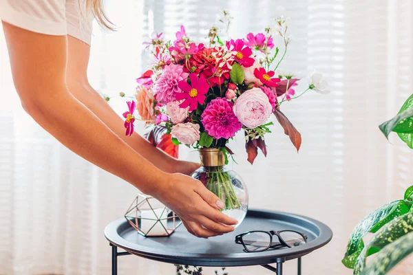 여자는 테이블에 꽃병에 꽃다발을 넣습니다 집에서 인테리어 아늑함과 장식을 돌보는 스톡 사진