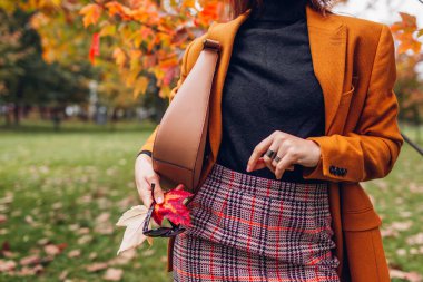 Güz parkında elinde çantasıyla turuncu ceketli mini etek takan şık bir kadının yaprak topladığı fotoğraf. Moda. Boşluk