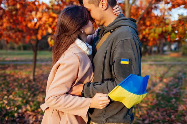 Ukrayna askeri üniformalı bayrak ve sembolle kocasıyla yüz yüze gelen bir kadın. Üzgün, vatansever çift dışarıda. Savaştan döndüm.