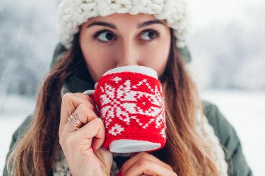 Karlı kış parkında kırmızı örgü Noel çantası giymiş sıcak çay fincanı içen bir kadın. Sıcak bir içecek.