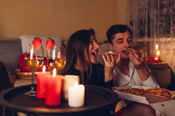 Valentines Day couple in love eating pizza drinking wine with strawberries having romantic dinner celebrating at home at night