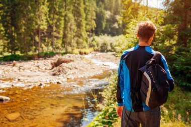 Sırt çantalı bir adam Karpat dağlarında ormanda yürüyüp huzurlu nehir manzarasının tadını çıkarıyor. Yazın Ukrayna 'da seyahat. Doğal manzara.