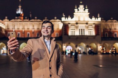 Yakışıklı adam Krakow Polonya 'daki pazar meydanında gece mimarlık yaparken selfie çekiyor. Tarihi yerleri ziyaret ederek Avrupa 'yı dolaşmak.
