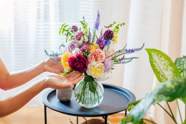Woman arranges bouquet of roses flowers in transparent vase on table. Taking care of interior and summer decor at home. Close up