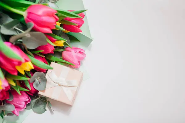 Spring flowers with gift box. Women\'s day background. Bouquet of yellow and pink tulips with ribbon. Present gift for Mother\'s day. Space. Top view