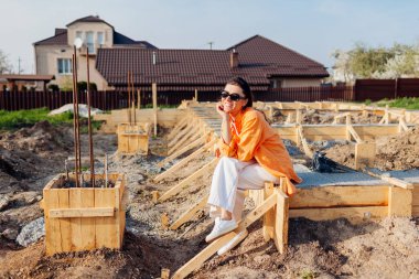 Yeni ev için beton temeli üzerine oturan mutlu bir kadın. Etrafı ahşap döşemelerle çevrili. Gelecekteki evin inşa edilmesini bekliyor..