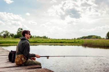 Askeri üniforma giymiş, balık tutan bir gencin vücut portresi. Köprüde oturan adam sırt çantasından çubuk tutuyor. Eğlence ve ruh sağlığı