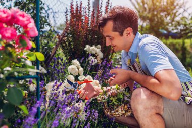 Boş kafalı adam yaz bahçesinde güller açıyor. Bahçıvan solmuş beyaz çiçekleri budayarak kesip metal sepete koyuyor..