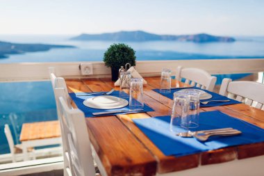 Yunanistan 'ın Santorini adasında servis edilen akşam yemeği masası, deniz kenarı ve dağların manzarası, volkan manzarası. Beyaz ahşap mobilyalar. Boş kafe