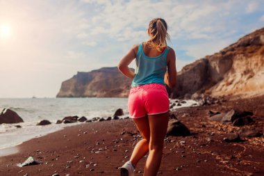 Santorini Adası 'ndaki Red Beach' te koşan kadının arka görüntüsü. Bayan koşucu dışarıda antrenman yaparken koşuyor ve manzaranın keyfini çıkarıyor. Sağlıklı sportif yaşam tarzı