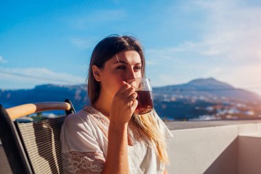 Otel terasında dinlenen bir kadın sabah kahvesini içip dağ manzarasının tadını çıkarıyor. Manzaralı kahvaltı. Yaz tatili