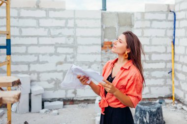 İnşaat halindeki evini kontrol eden mutlu genç bir kadın binanın içindeki planla karşılaştırma yapıyor. Geleceğin sahibi rahat bir ev hayal ediyor.