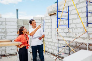 Erkek mimar mühendis inşaat halindeki evi müstakbel ev sahibine gösteriyor. Planı kontrol ediyor. Proje sırasında gaz bloğu oluşturulurken danışmanlık