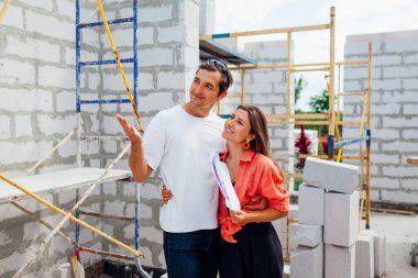 Mutlu genç çift inşaat halindeki müstakbel evlerini kontrol ediyor. Aile, evlerini gaz bloğundan yapılmış duvarın yanında elinde kağıt planları tutarken hayal ediyor.