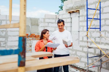 Mutlu genç çift inşaat halindeki müstakbel evlerini kontrol ediyor. Aile, evlerini gaz bloğundan yapılmış duvarın yanında elinde kağıt planları tutarken hayal ediyor.