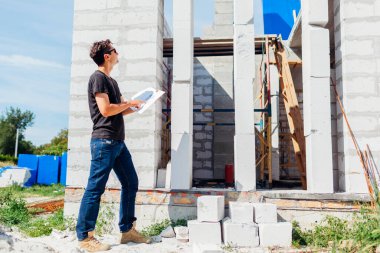 İnşaat halindeki evi kontrol eden mimar adam kağıt üzerindeki planla karşılaştırıyor. İşçi dışarıdaki pencere boşluğuna bakıyor