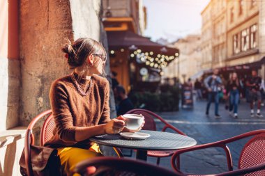 Cafe 'de oturmuş kahve içen şık bir kadının portresi. Lviv şehrinin mimarisinden hoşlanan bir kadın sonbahar günü caddede