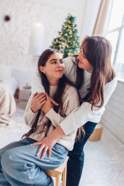 Anne evde süslenmiş Noel ağacıyla kızına sarılıyor. Tatil kışı iç kısımları. Mutlu aile şenlik stüdyosunda poz veriyor.